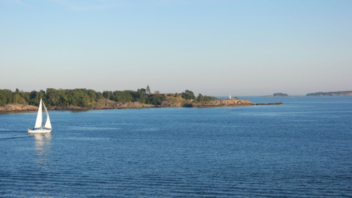 A small sailing boat on a calm sea gliding between islands.