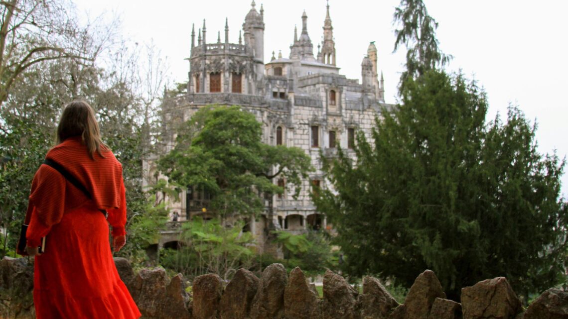 Woman in red dress walking in a park towards a stone castle.