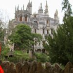 Woman in red dress walking in a park towards a stone castle.